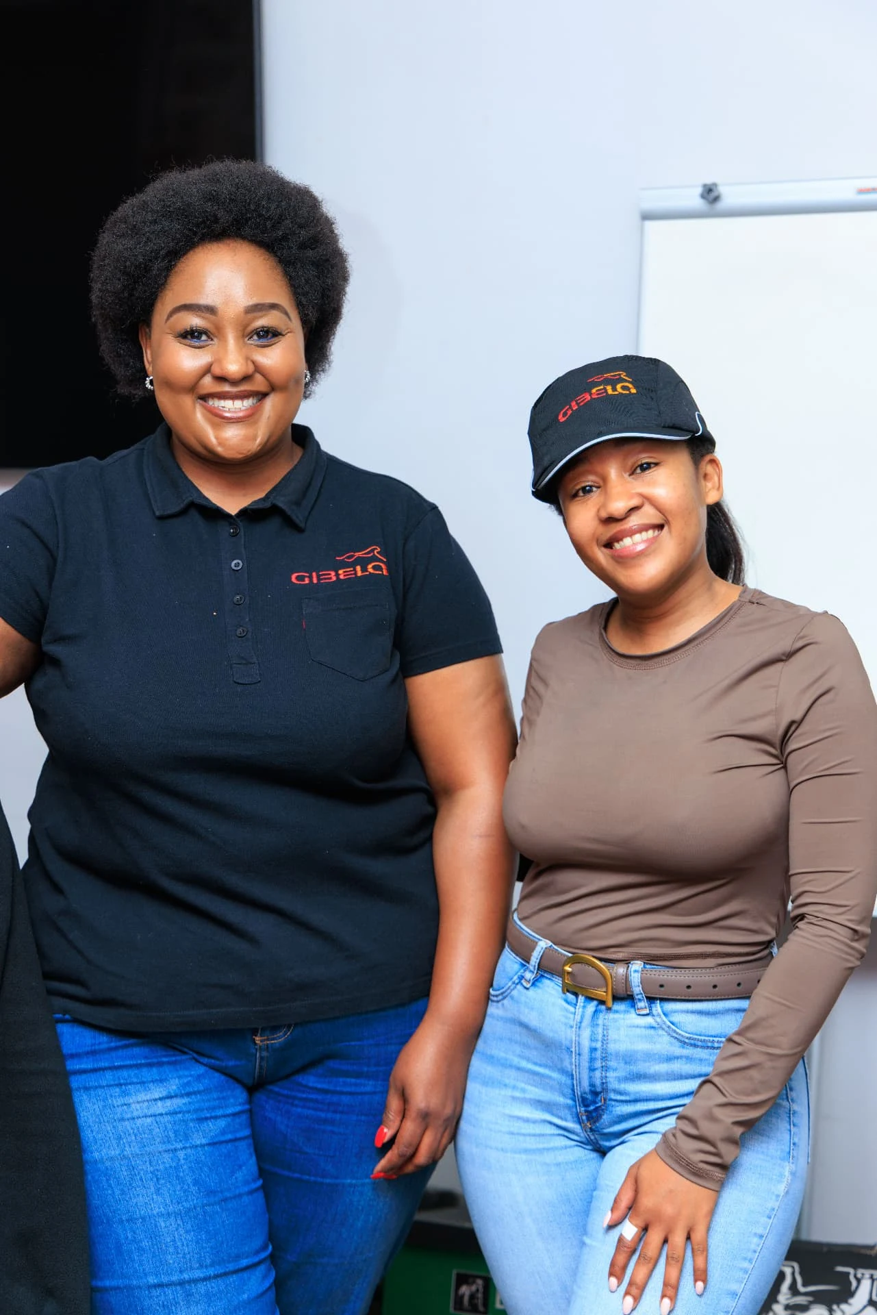 Two attendees posing together, with Gibela branding visible on a polo shirt and cap.