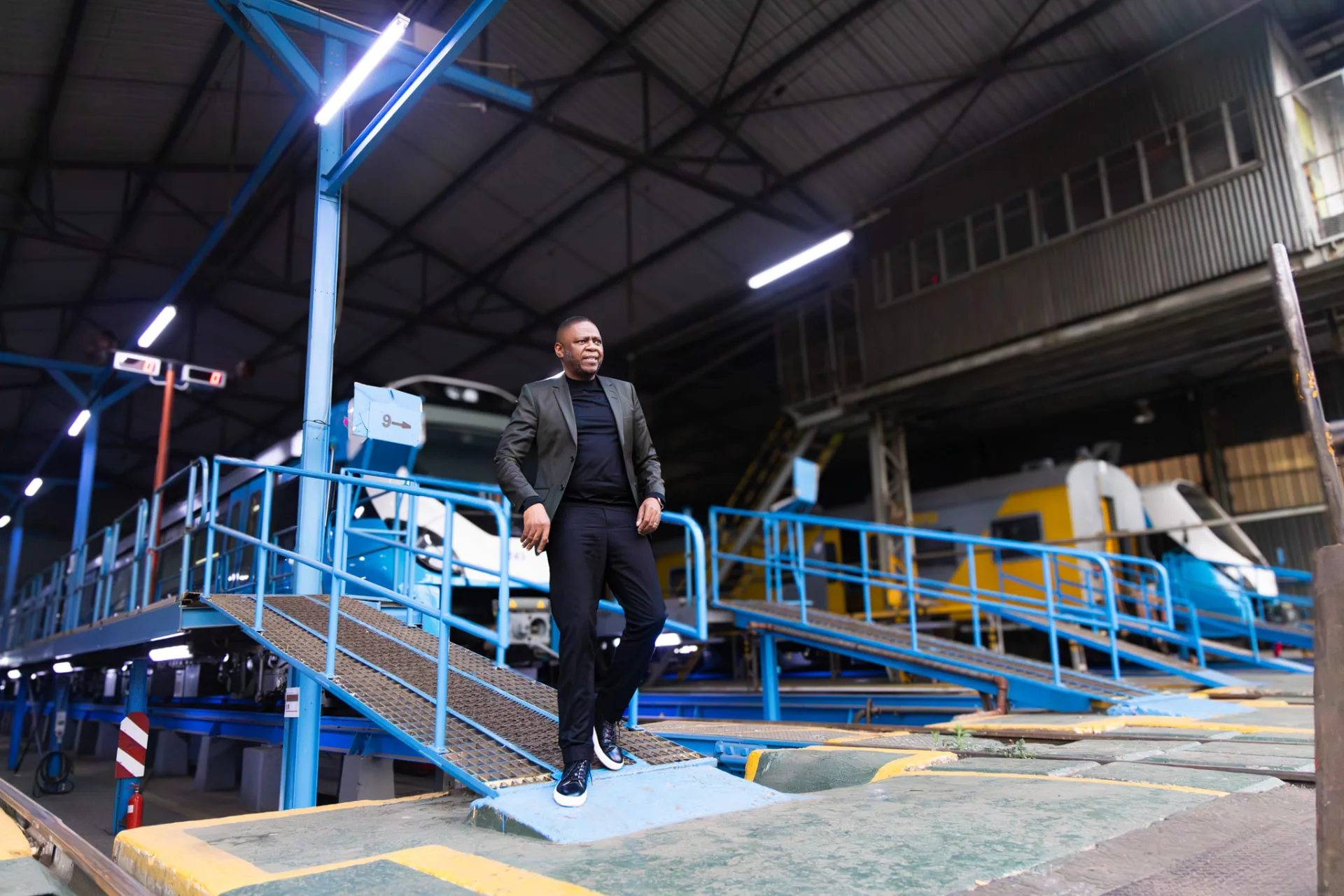 Mr Themba Mosai stepping down from a depot ramp with trains in the shed behind him.