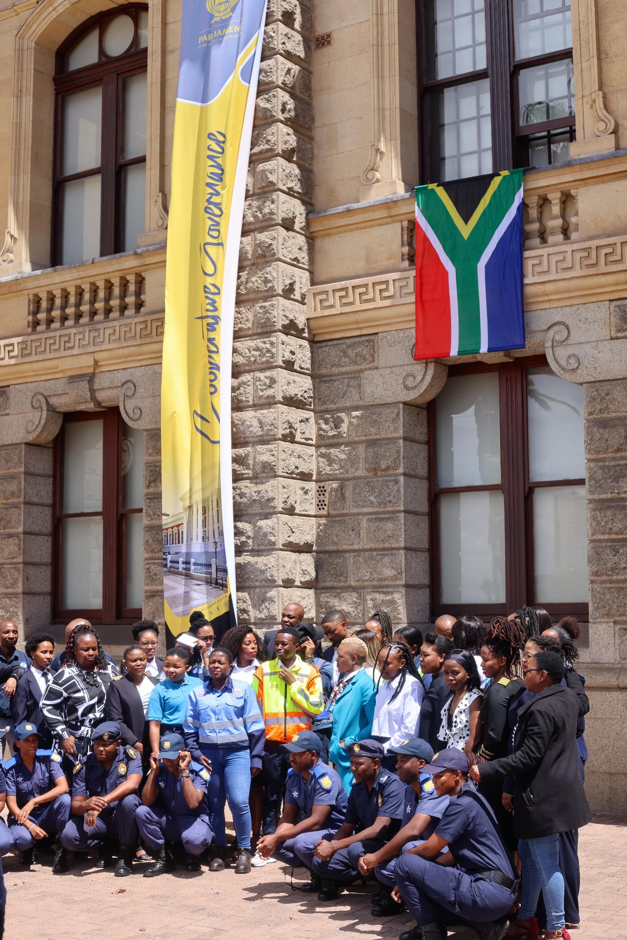 Group gathering beneath the Parliament banner and South African flag
